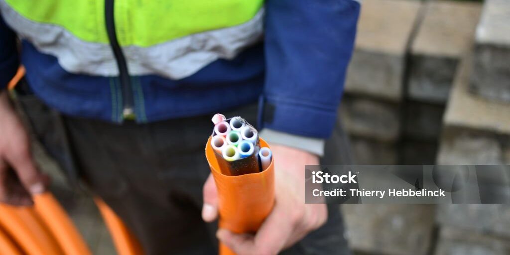 fiber-optics-is-2047935663-1024x1024 Supervisory road worker shows 9 hollow tubes in an orange pipeline used to blow in fiber optic wires. 2 outdoor pipes used for connection to the house